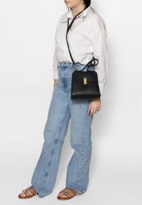 Borsa a tracolla in pelle nera con dettagli dorati, forma rettangolare e tracolla regolabile. Abbinata a jeans a vita alta blu chiaro e sandali con cinturini.