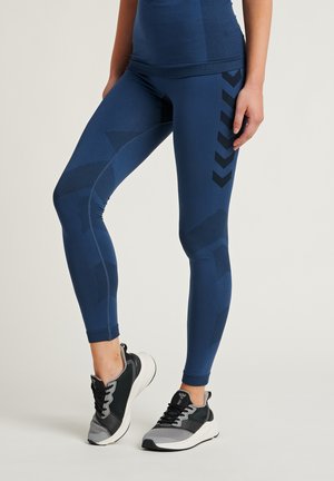 Marineblauwe leggings met textuurpatronen en zwarte accenten, aansluitend ontwerp, aangevuld met grijze en zwarte sportchoenen.