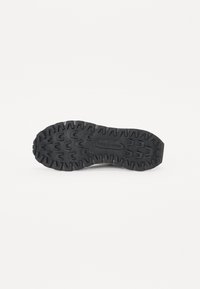 Svart gummisåle med dype spor og teksturert overflate, med hevede mønstre for grep, merket med "Merrell"-logo.