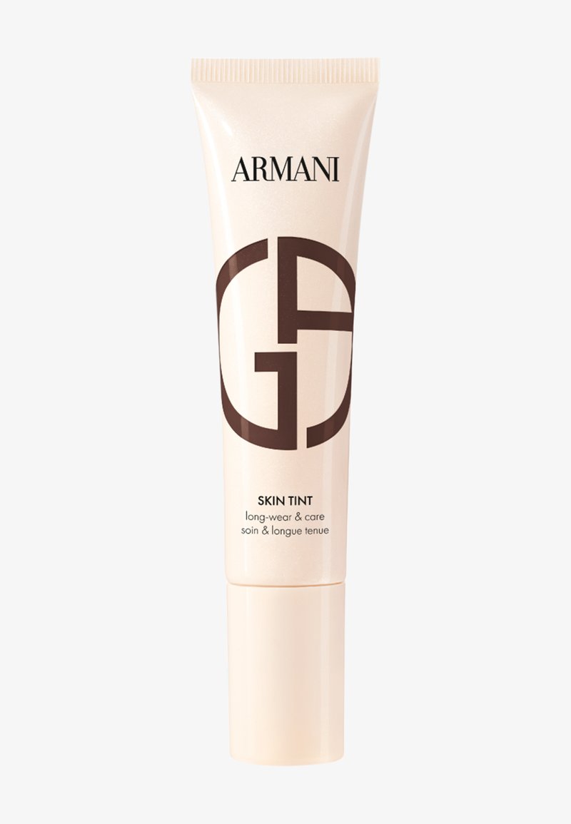 Beige Tube von Armani Skin Tint mit dunklem braunem Logo, zylindrischer Form und glänzender Oberfläche. Der Text enthält "langanhaltend & pflegend."