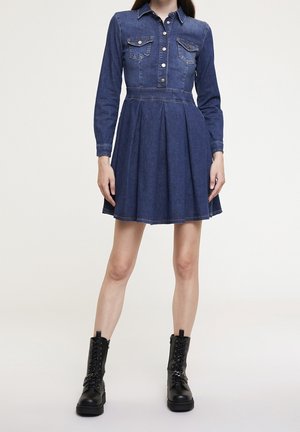 Woman wearing a blue denim long-sleeve dress with button-down front and black lace-up boots with chain details.