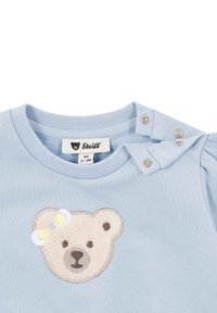 T-shirt di cotone azzurro chiaro con motivo orsetto, caratterizzata da un volto ricamato in rilievo e un piccolo fiocco. Chiusure a pressione sulla spalla.