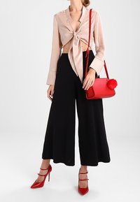 Jasnoróżowa satynowa bluzka zawiązywana z przodu na kokardę, czarne spodnie o szerokich nogawkach, czerwona torebka z pomponem oraz czerwone sandały na wysokim obcasie z paskami.