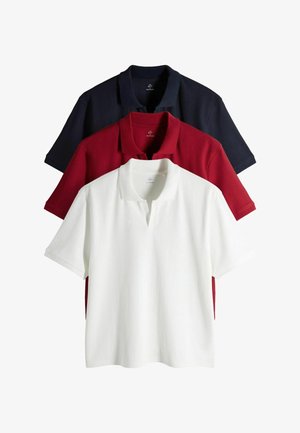 Trīs ribotas polo kreklas sakārtotas kaudzē, krāsās — balts priekšā, sarkans vidū un melns aizmugurē, ar īsām piedurknēm un atvērtu apkakli.