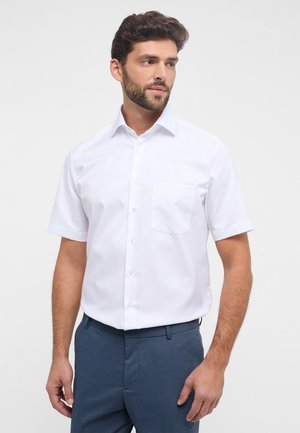 Camicia bianca in cotone a maniche corte con chiusura a bottoni frontale e taschino sul petto, caratterizzata da un colletto classico e una superficie liscia e uniforme.