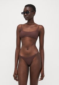 Brunstripete bikini med tynne stropper og minimal dekning. Stoffet ser glatt og elastisk ut, designet for svømmetøy.