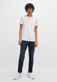 Hvid bomulds t-shirt med rund hals, kombineret med mørkeblå denim jeans og hvide sneakers. Glat tekstur, afslappet pasform.
