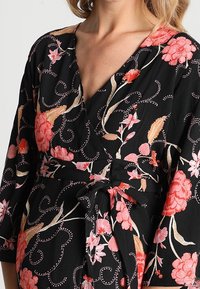 Schwarzes Wickelkleid mit lebhaften Blumenmustern in Pink, Rot und Beige, cinch-tailliert und mit dreiviertel Ärmeln.