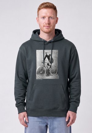 Mann trägt dunkle Kapuzenjacke mit schwarz-weißem Aufdruck eines Radfahrers auf einem Vintage-Fahrrad und Text "No Gears. No Limits."