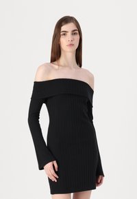 Vestido preto canelado, com ombros à mostra e mangas compridas, de corte justo que destaca um tecido texturizado e um comprimento subtil.