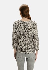 Top w print zwierzęcy, z beżowym tłem i czarnymi paskami tygrysa, długimi rękawami z marszczonymi mankietami oraz luźnym krojem.