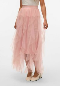 Gonna midi in tulle rosa chiaro con volant sovrapposti, vita liscia e tessuto fluido, abbinata a calzature chiare.