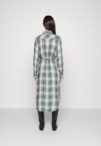 Dlouhé kárované šaty v zelených a modrých tónech, vyrobené z lehké látky. Mají pás v pase a zapínané manžety, límec a boční rozparky.