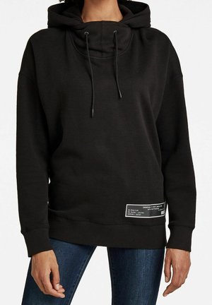Sweatshirt à capuche noire avec un col montant, des cordons de serrage ajustables et une étiquette bien visible sur l'ourlet inférieur. Tissu doux et coupe décontractée.