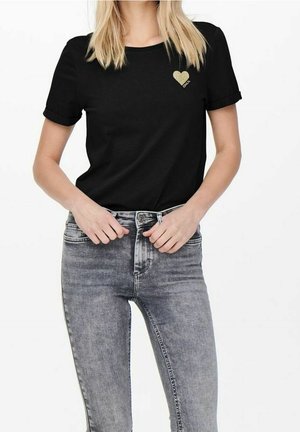 Zwart katoenen T-shirt met opgerolde mouwen en een goud hartontwerp op de linkerborst, gecombineerd met grijze skinny jeans.