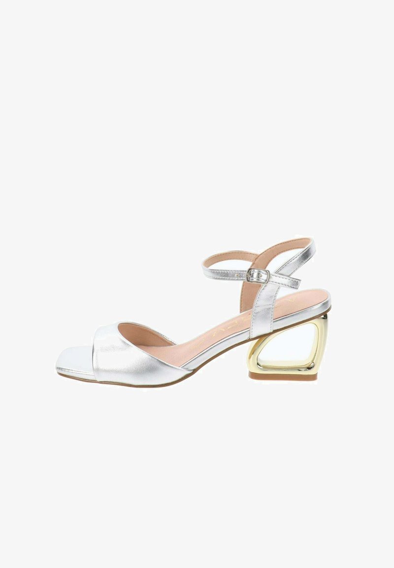 Sandal aperto argento metallico con cinturino alla caviglia, caratterizzato da un tacco geometrico a blocco dorato a contrasto e una superficie liscia.