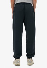 Pantalones de chándal negro marino con cintura elástica y puños acanalados, hechos de una tela suave. Combinados con zapatillas deportivas de colores claros.