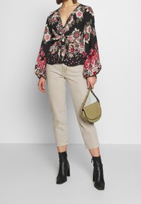 Black floral blouse with puffy sleeves, knotted front detail, cream tapered jeans, and black heeled ankle boots. Olive green crossbody bag.