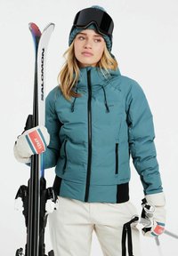 Teal isolierte Skijacke mit Reißverschlusstaschen, schwarzen Akzenten und Kapuze mit Kordelzug. Weiße Skihandschuhe mit roten, blauen und grünen Streifen.
