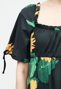 Μαύρο φόρεμα με φουσκωτά μανίκια και πράσινο και κίτρινο λουλουδένιο μοτίβο, τετράγωνο ντεκολτέ με διακοσμητικό βολάν και δετή λεπτομέρεια στο μανίκι.
