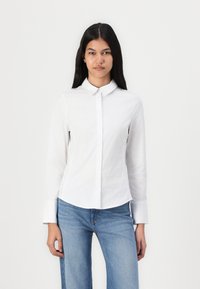 Cămașă albă cu guler, cu mâneci lungi și tiv curbat. Poartă cu blugi din denim albastru. MaterialNeted și ușor.
