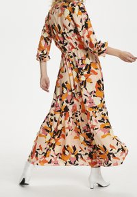 Lange, bloemenmaxi-jurk in oranje, roze, zwart en crèmekleuren. Heeft een ontspannen pasvorm, een elastische taille en een gelaagde ruffle zoom. Witte hoge laarzen.