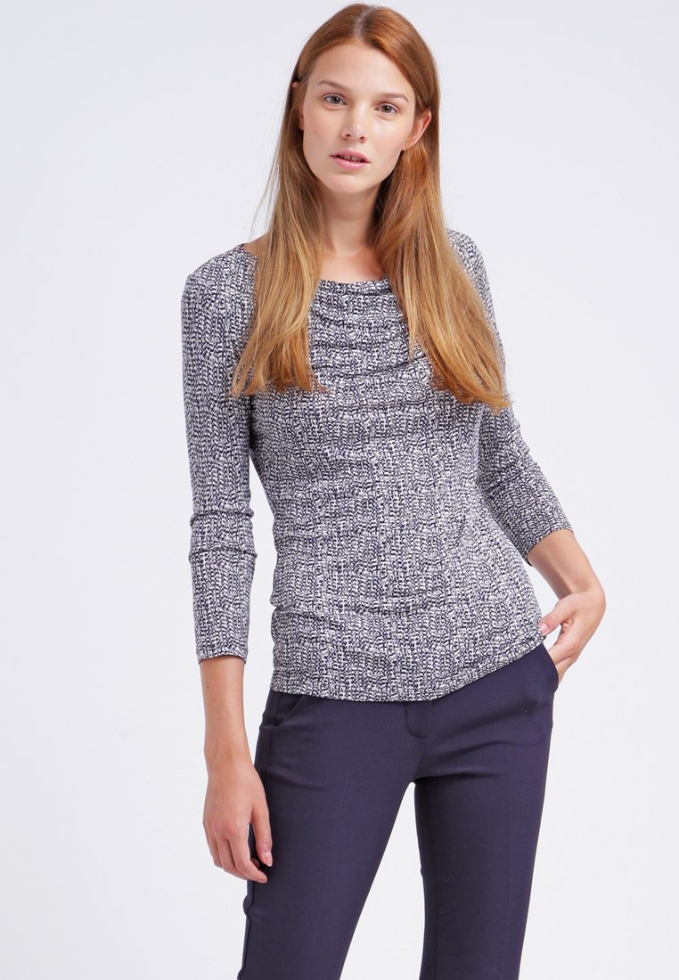 Haut à manches longues avec un motif texturé bleu marine et blanc, présentant un col rond et une coupe ajustée. Associé à un pantalon sombre.