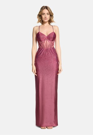 Vrouw in een satijnen galajurk tot op de vloer, zonder mouwen, in diep roze met een doorschijnend en met kralen versierd lijfje, staand tegen een effen witte achtergrond.