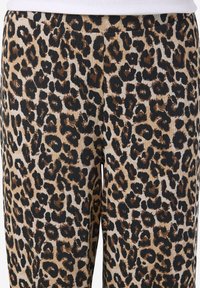 Μπεζ ριμπ παντελόνι με καφέ και μαύρο λευκοθησαυρό μοτίβο, φορεμένο με λευκό μπλουζάκι μέσα στην παντελόνα.