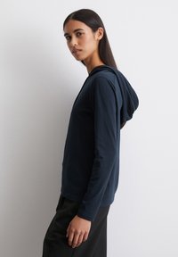 Marineblauwe hoodie met lange mouwen, gemaakt van zachte stof, met een ronde onderkant en een voorzak, in een losse pasvorm en een verstelbare trekkoordcapuchon.