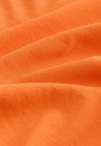 Weicher orangefarbener Stoff mit sichtbarer gewebter Struktur und sanften Falten, die subtile Schatten und Tiefe erzeugen.