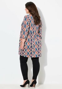 Tunika colorata a fantasia in tonalità di blu, arancione e rosso, con un design svasato, abbinata a leggings neri e tacchi alti neri.