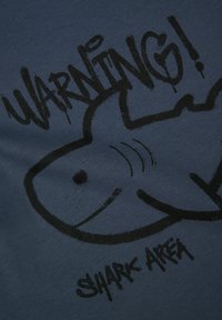 Námorně modré tričko s velkým černým grafikou žraloka a textem "POZOR! ZÓNA ŽRALOKŮ" tučným, opotřebovaným písmem.