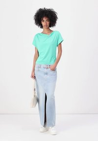 Top a maniche corte verde menta con scollatura drappeggiata e dettaglio argentato abbinato a una gonna maxi in denim azzurro chiaro a vita alta con spacco frontale.