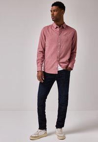 Maglietta a maniche lunghe a righe rosse e bianche con bottoni, abbinata a jeans in denim scuri e sneakers chiare. Il tessuto sembra di tipo cotone con una superficie liscia.