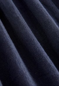 Navy puuvillakangas hienolla neulepinnalla, jossa on hienovaraisia, rinnakkaisia viivoja ja sileä ulkonäkö, taittuneena pehmeisiin aaltoihin.