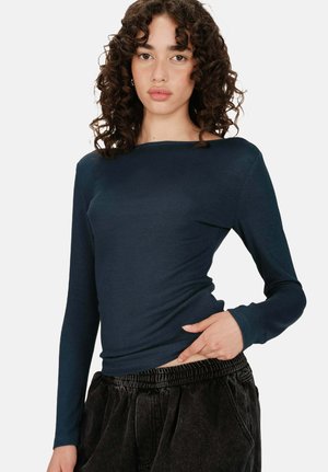 Haut en ribbed bleu marine à manches longues avec un col bateau, une coupe ajustée et une texture douce. Assorti à un pantalon foncé ample avec une taille élastique.