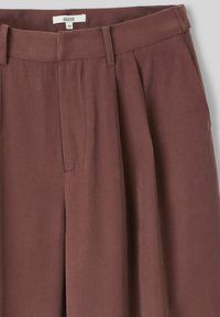 Pantalons marron plissés en tissu doux avec une texture lisse. Comprend une étiquette à la taille, une assise avant et une coupe ajustée.