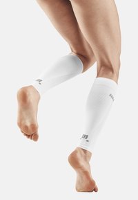 White compression calf sleeves featuring a textured design and gray logo accents, covering the lower leg up to the knee.