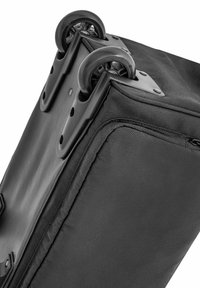 Czarna torba na kółkach w kształcie prostokąta, wykonana z trwałego materiału. Posiada gładkie, duże czarne kółka oraz widoczne detale w postaci szwów.