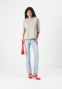 Lys grå oversized t-skjorte, lys blå rett ben jeans, røde hæler med spiss tupp og matchende rød håndveske. Enkelt design, avslappet stil.