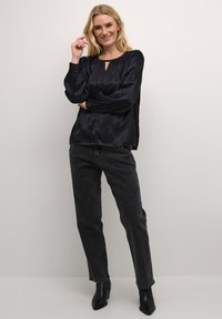 Mustmust blouse, millede õlavarre avausega ja pikkade varrukatega, koos kõrge vöökohaga hallide teksade ja pahkluu saapatega. Minimalistlik disain.