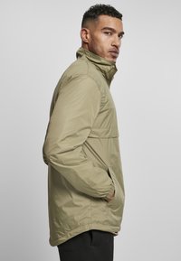 Khaki letvægtsjakke med høj krave, lynlås foran og sidelommer med elastiske manchetter. Glat, vandafvisende stoffinish.
