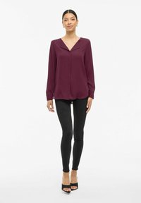 Blusa bordeaux a maniche lunghe con colletto a punte, abbinata a jeans skinny neri e tacchi open-toe neri. Tessuto con finitura liscia.