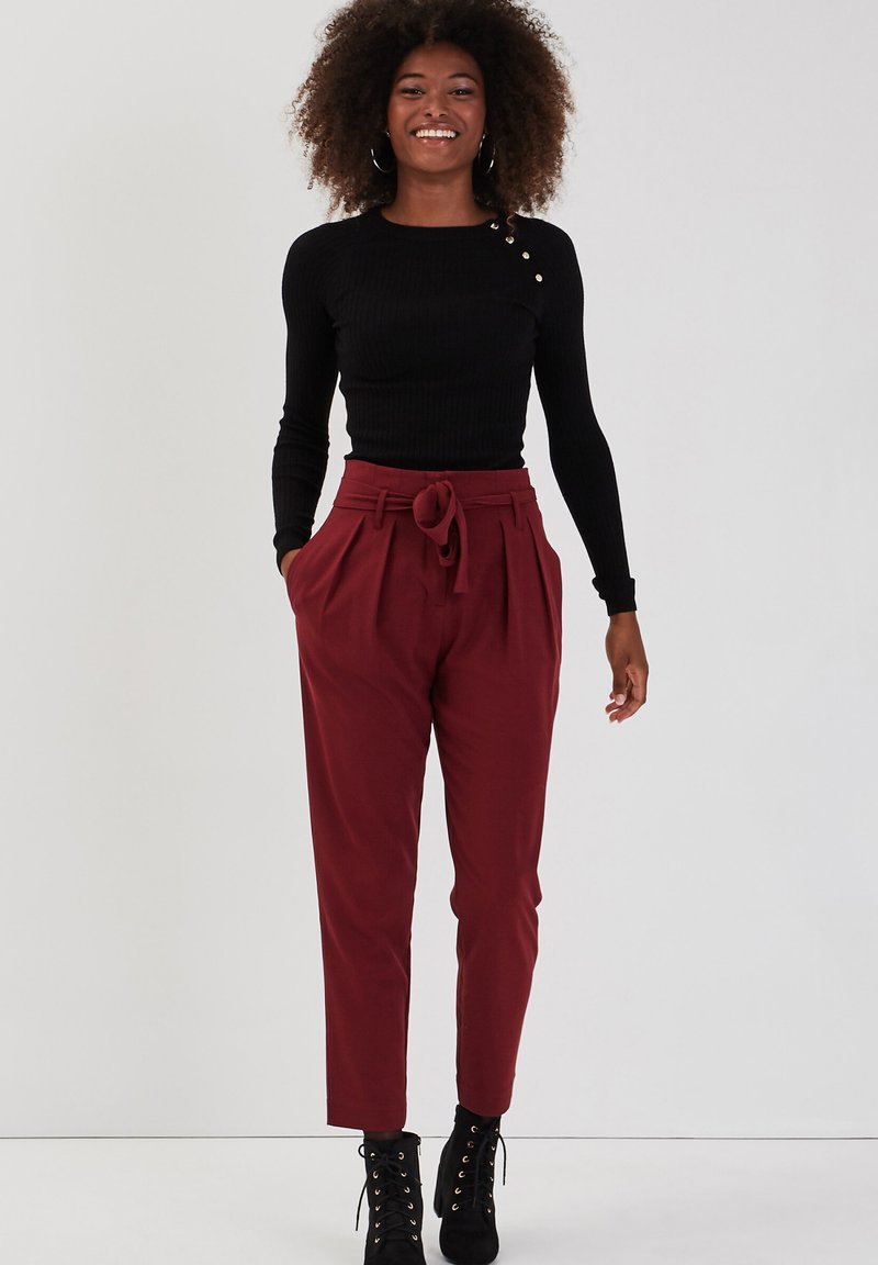 Haut noir à manches longues côtelé avec détail de boutons, associé à un pantalon bourgogne taille haute avec une taille nouée. Porté avec des bottes noires à lacets.