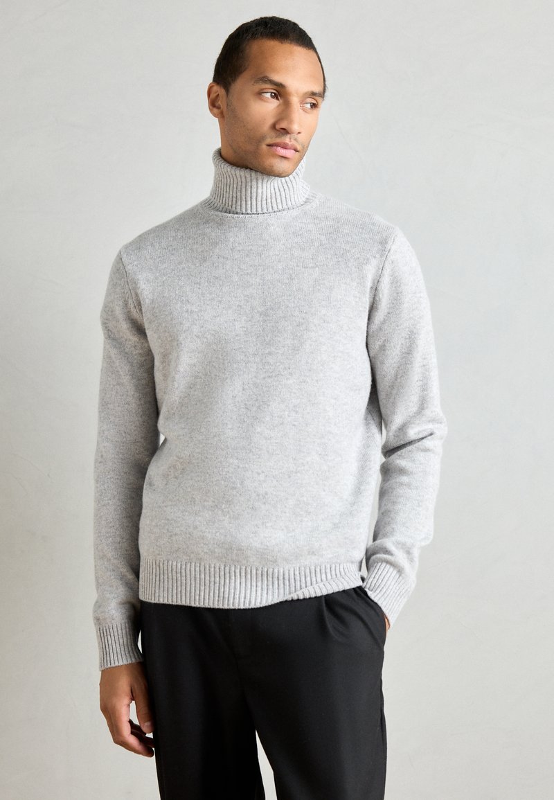 Pull col roulé gris clair en tissu tricoté doux. Doté de manches et d'un ourlet côtelés. Assorti à un pantalon noir.