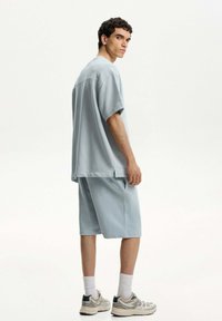 Világoskék, oversize póló és hozzá illő short, puha anyagból készült. Rövid ujjú, lazán illeszkedő, oldalsó zsebekkel, futócipővel párosítva.
