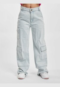 Pantalones cargo azul claro con piernas anchas, dos grandes bolsillos laterales y cierre frontal con botón. Cuenta con bordado KANJE en la pierna izquierda.