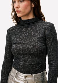 Zwarte top met lange mouwen en hoge hals, voorzien van een getextureerd bloemenpatroon. Gecombineerd met metalen zilverkleurige hoge taille broek.