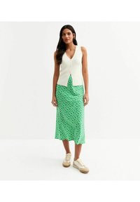 Top en jersey côtelé crème sur une jupe maxi florale verte, associé à des baskets beiges. L'ensemble présente des détails de boutons et des textures lisses.